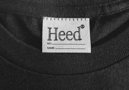 A black HEED ESSENTIALS Tee featuring the iconic Heed logo on the sleeve. The tee is crafted from premium Japanese cotton, with a mental health focus and a unisex fit. The design is simple and versatile, suitable for various occasions. From your Mental Health and Self Care Streetwear Clothing Brand.